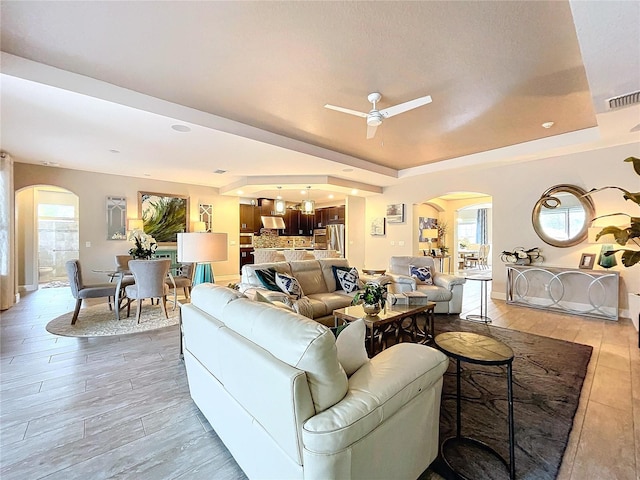 living area featuring arched walkways, a raised ceiling, and plenty of natural light