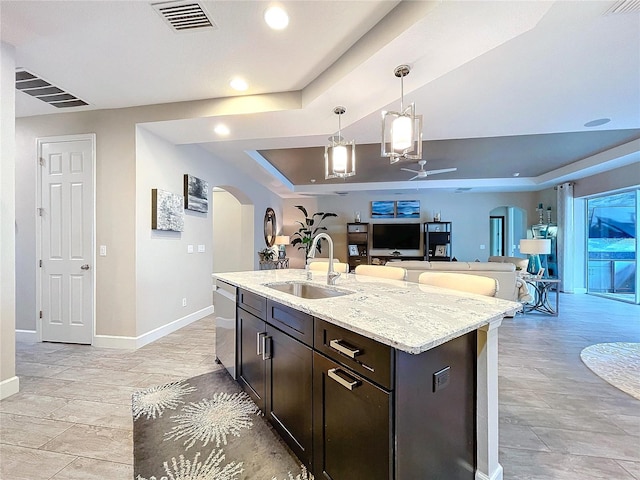 kitchen with arched walkways, a sink, open floor plan, stainless steel dishwasher, and a raised ceiling