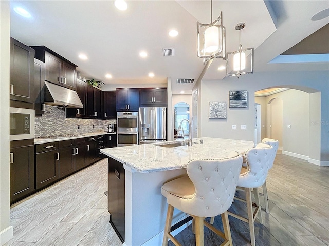 kitchen with arched walkways, visible vents, appliances with stainless steel finishes, a sink, and under cabinet range hood