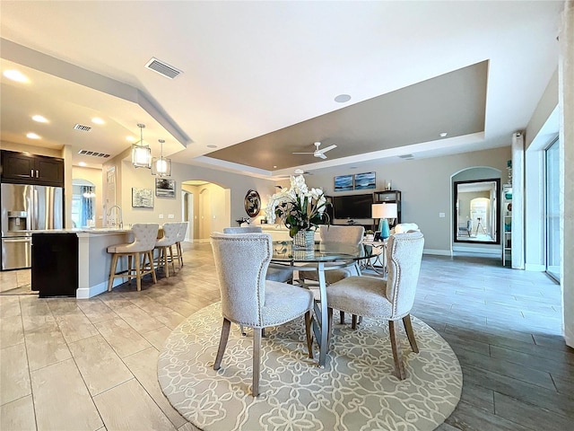 dining area featuring visible vents, wood tiled floor, arched walkways, and a tray ceiling