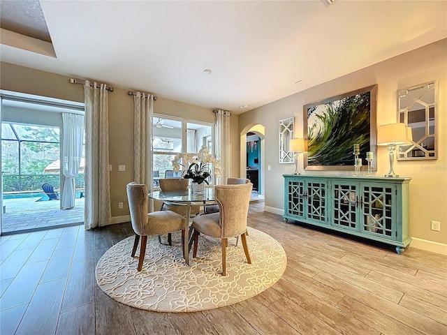 dining room featuring arched walkways, plenty of natural light, baseboards, and wood finished floors