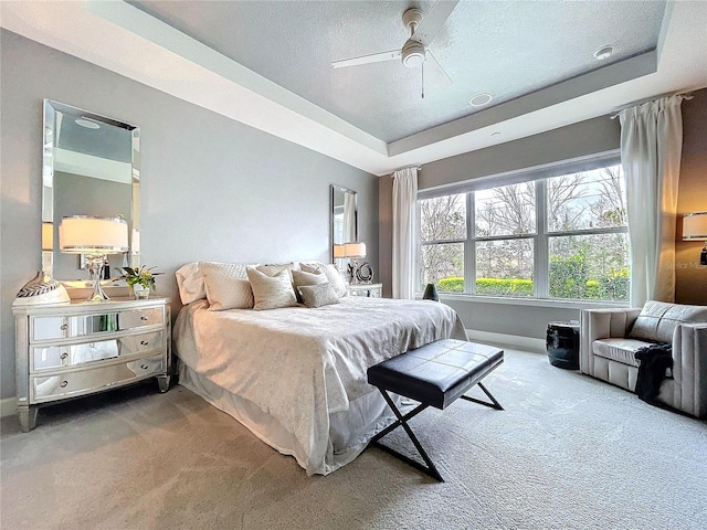 bedroom featuring baseboards, ceiling fan, carpet, a tray ceiling, and a textured ceiling