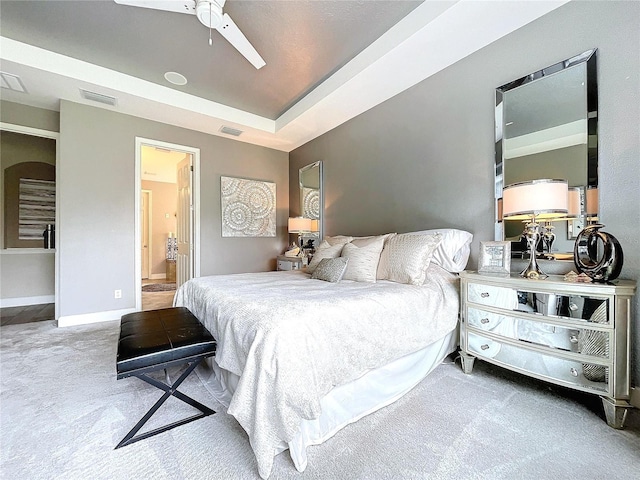 carpeted bedroom with baseboards, connected bathroom, visible vents, and a tray ceiling