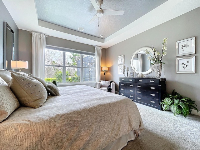 bedroom featuring a textured ceiling, carpet, a raised ceiling, and a ceiling fan