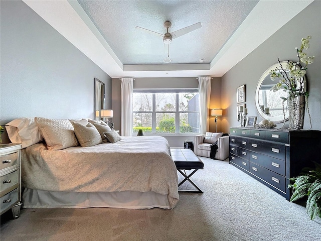 carpeted bedroom with a ceiling fan, a raised ceiling, and a textured ceiling