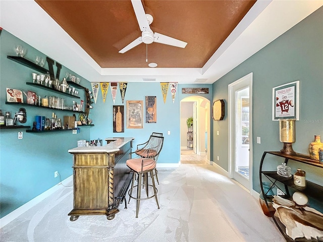 bar featuring arched walkways, light carpet, baseboards, a dry bar, and a raised ceiling