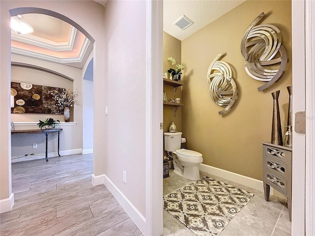 bathroom featuring baseboards, visible vents, toilet, wood finished floors, and a tray ceiling