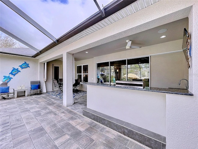 view of patio / terrace featuring glass enclosure, outdoor dry bar, and a ceiling fan