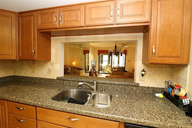 kitchen with tasteful backsplash, sink, a notable chandelier, and dark stone counters