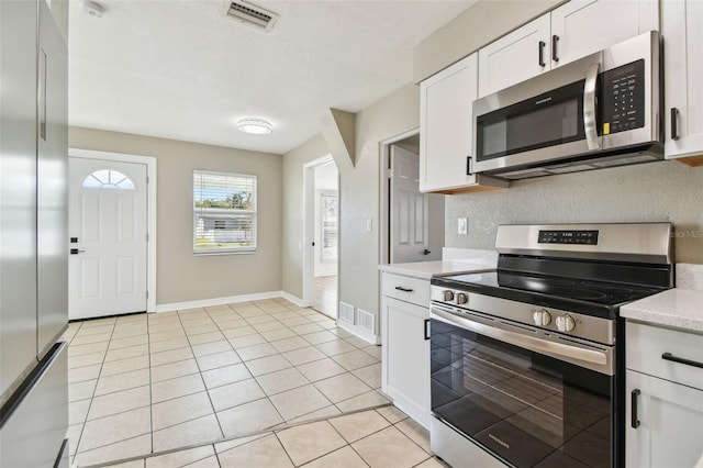 kitchen with light tile patterned flooring, white cabinetry, a textured ceiling, appliances with stainless steel finishes, and backsplash