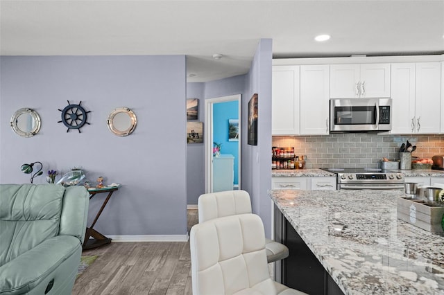 9911 Antilles Dr, Seminole, FL 33776 - kitchen with white cabinets, light wood-style flooring, stainless steel appliances, and decorative backsplash