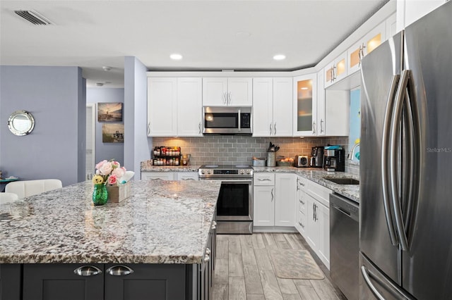 9911 Antilles Dr, Seminole, FL 33776 - kitchen with visible vents, glass insert cabinets, light stone countertops, stainless steel appliances, and white cabinetry