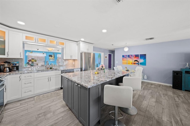 9911 Antilles Dr, Seminole, FL 33776 - kitchen with a breakfast bar, a center island, stainless steel appliances, glass insert cabinets, and white cabinetry