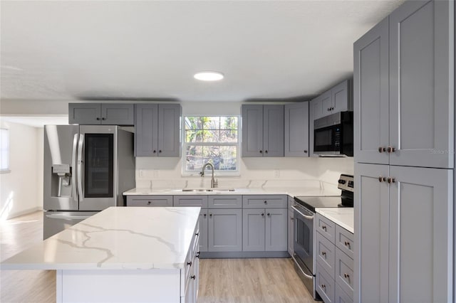 kitchen with sink, light stone counters, light hardwood / wood-style flooring, appliances with stainless steel finishes, and a kitchen island