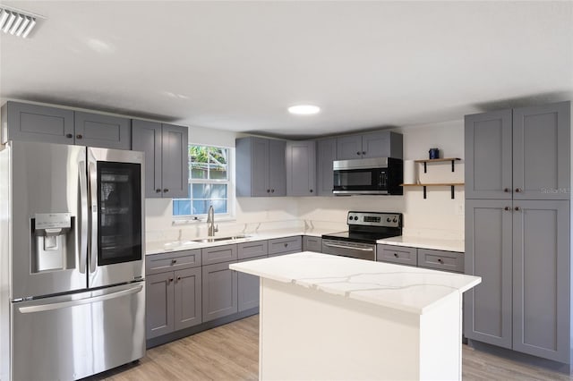 kitchen with stainless steel appliances, a center island, sink, and gray cabinetry