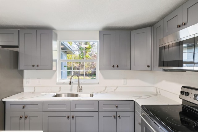 kitchen featuring sink, gray cabinetry, a textured ceiling, appliances with stainless steel finishes, and light stone countertops