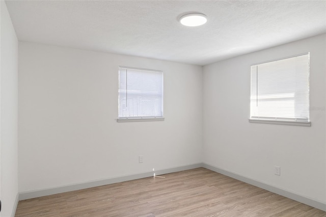 empty room featuring a healthy amount of sunlight, a textured ceiling, and light wood-type flooring