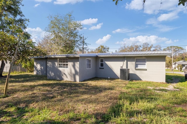 rear view of property with central AC unit and a lawn