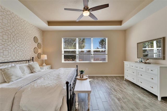 bedroom with ceiling fan, light hardwood / wood-style floors, and a raised ceiling