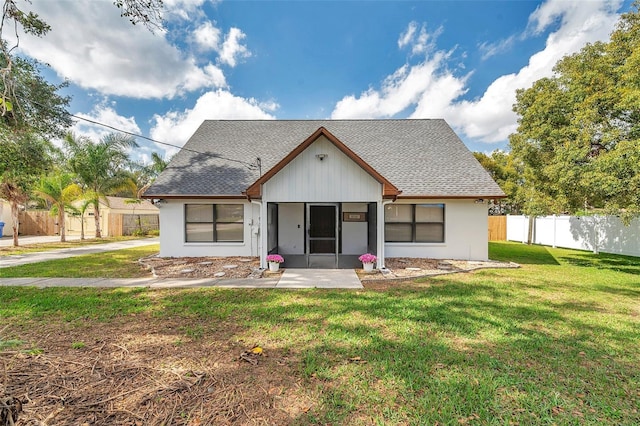 view of front facade featuring a shingled roof, fence, a front lawn, and a patio