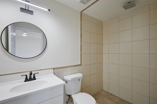 bathroom featuring vanity, a tile shower, tile walls, and toilet