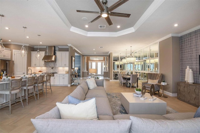 living room featuring sink, crown molding, ceiling fan, a tray ceiling, and a textured ceiling