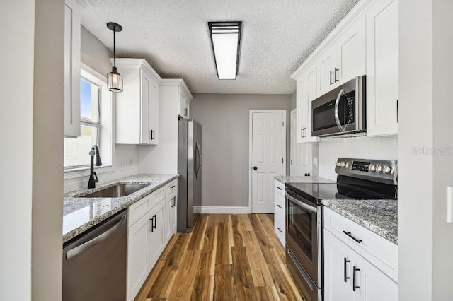 kitchen with stainless steel appliances, wood finished floors, a sink, white cabinetry, and backsplash