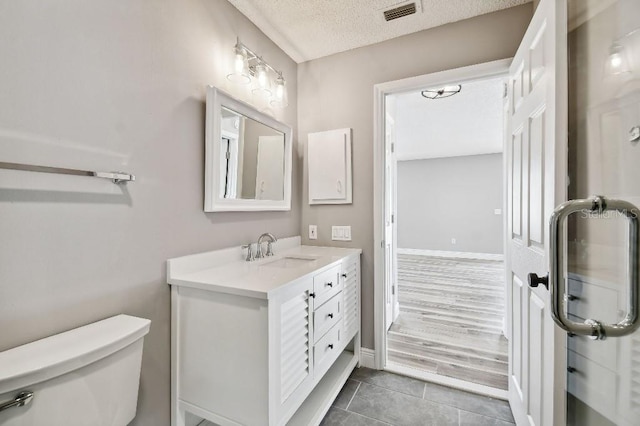 bathroom with a textured ceiling, tile patterned flooring, toilet, vanity, and visible vents