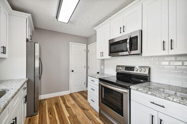 kitchen featuring stainless steel appliances, a textured ceiling, light wood-type flooring, white cabinetry, and backsplash