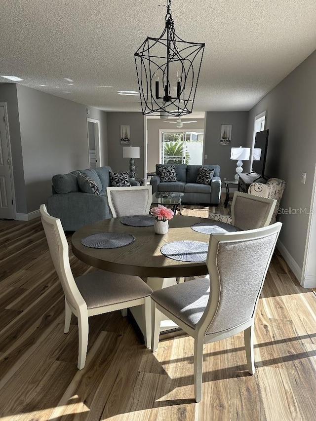 dining space featuring an inviting chandelier, a textured ceiling, baseboards, and wood finished floors