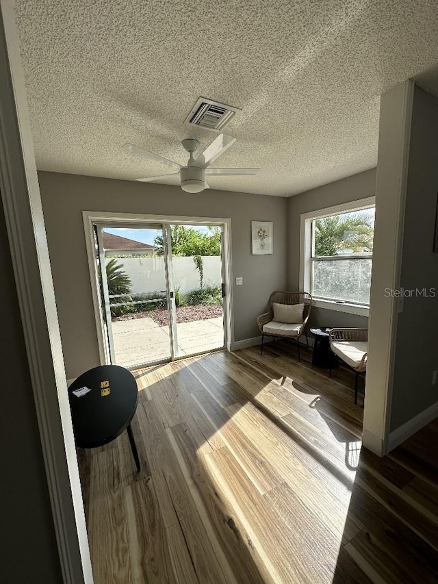 living area with visible vents, a ceiling fan, a textured ceiling, wood finished floors, and baseboards