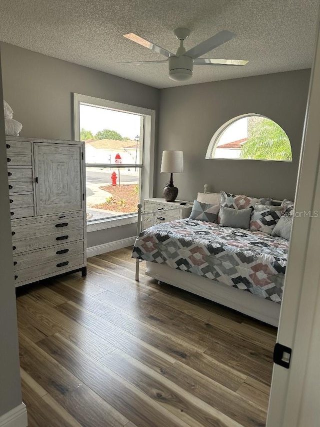 bedroom featuring ceiling fan, a textured ceiling, baseboards, and wood finished floors