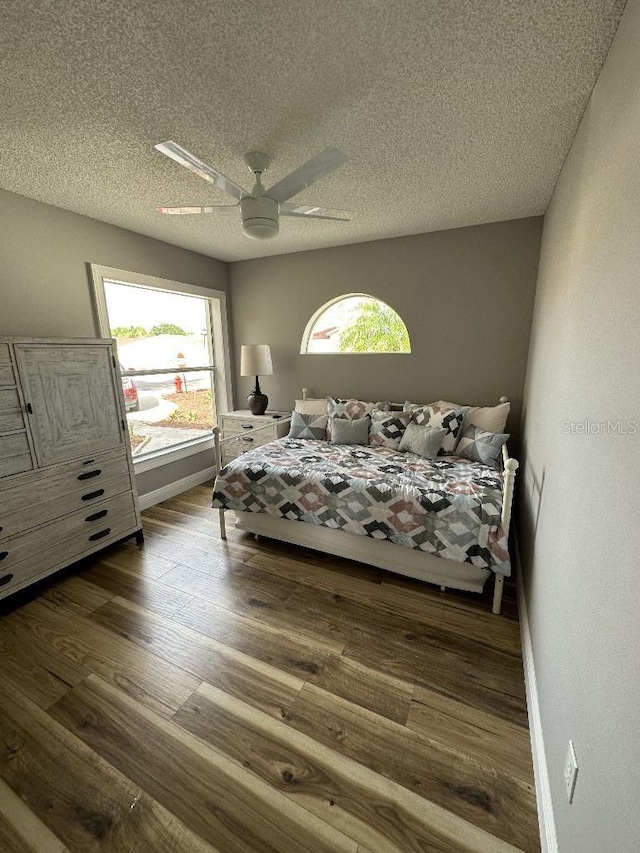 unfurnished bedroom with a ceiling fan, multiple windows, a textured ceiling, and wood finished floors