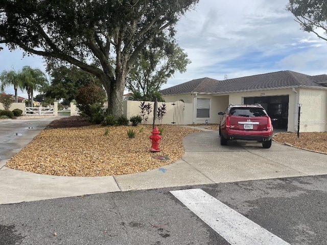 ranch-style home with driveway, an attached garage, a gate, fence, and stucco siding