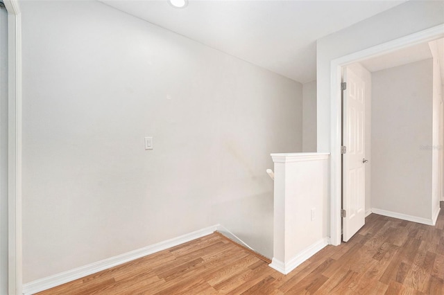 corridor featuring baseboards, wood finished floors, and an upstairs landing