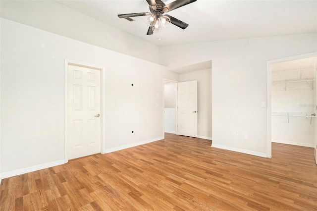 unfurnished bedroom featuring light wood finished floors, baseboards, lofted ceiling, ceiling fan, and a walk in closet