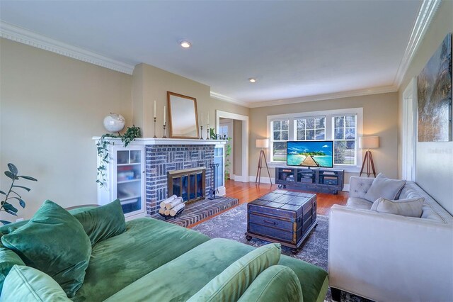 living area with recessed lighting, wood finished floors, baseboards, a brick fireplace, and crown molding