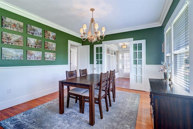 dining area with a wainscoted wall, plenty of natural light, an inviting chandelier, and wood finished floors