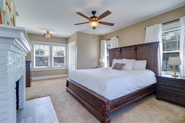 bedroom with a brick fireplace, multiple windows, and light colored carpet