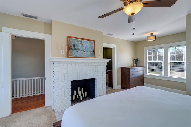 bedroom with a brick fireplace, carpet, visible vents, and ceiling fan