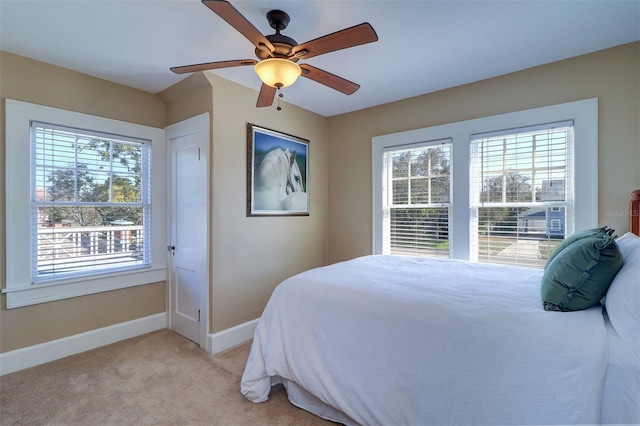 bedroom featuring a ceiling fan, light carpet, baseboards, and multiple windows