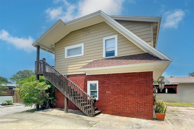 view of side of home featuring roof with shingles, brick siding, and stairway