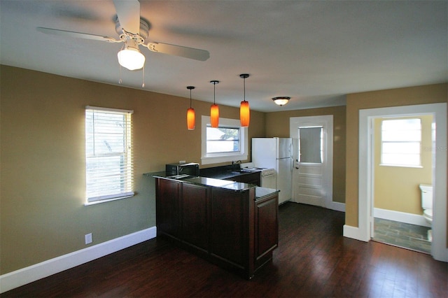 kitchen featuring dark wood-style flooring, hanging light fixtures, freestanding refrigerator, a peninsula, and baseboards