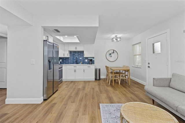 interior space featuring tasteful backsplash, light wood-type flooring, white cabinets, and appliances with stainless steel finishes