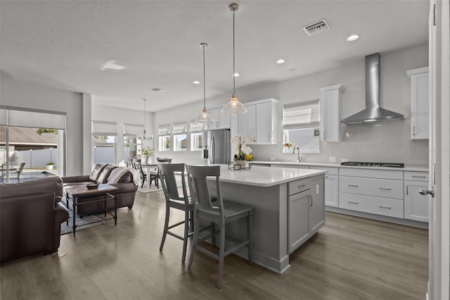 kitchen featuring wall chimney exhaust hood, white cabinetry, decorative light fixtures, a center island, and stainless steel appliances