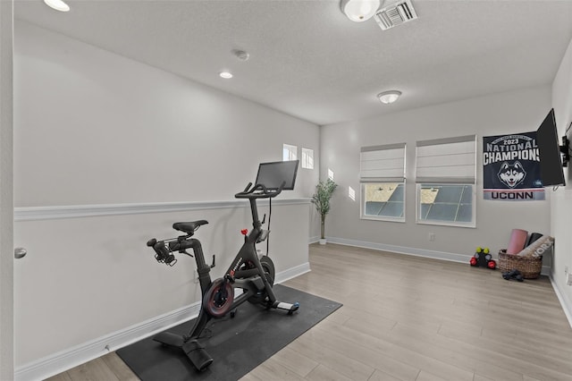 workout room with a textured ceiling and light wood-type flooring