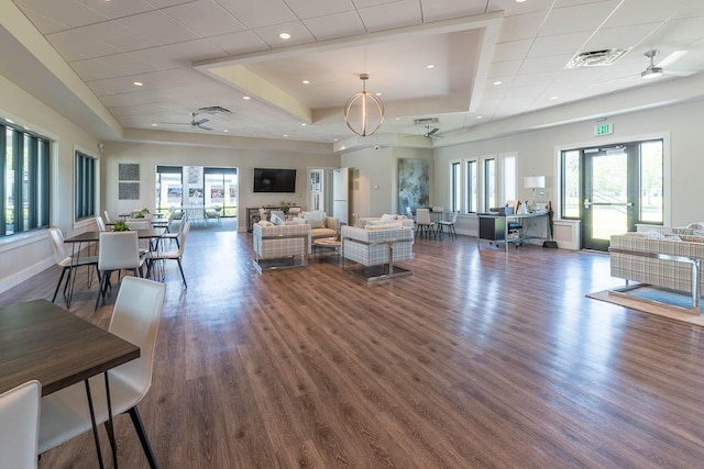 living room featuring a raised ceiling, dark wood-type flooring, and ceiling fan