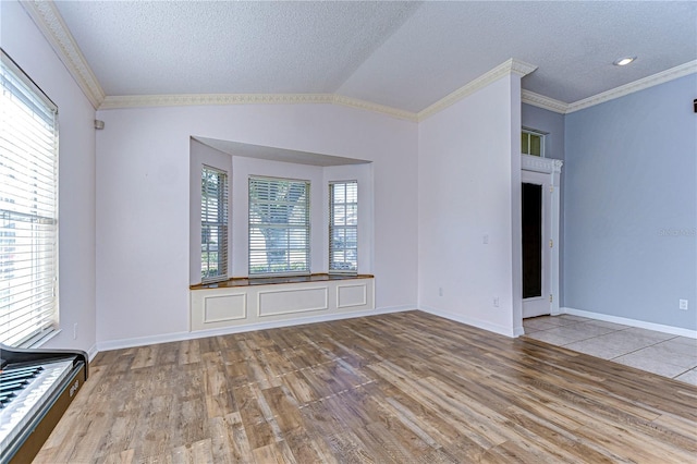 spare room featuring ornamental molding, lofted ceiling, a textured ceiling, and light hardwood / wood-style floors