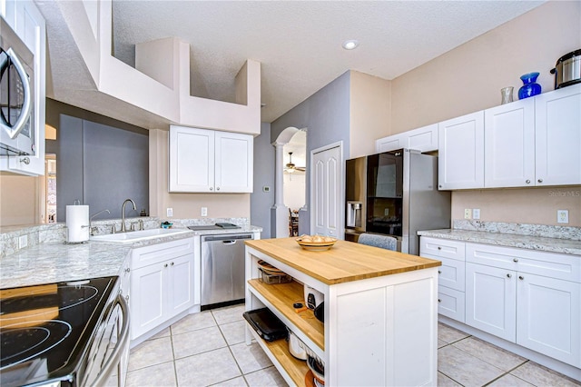 kitchen with sink, light tile patterned floors, stainless steel appliances, light stone countertops, and white cabinets