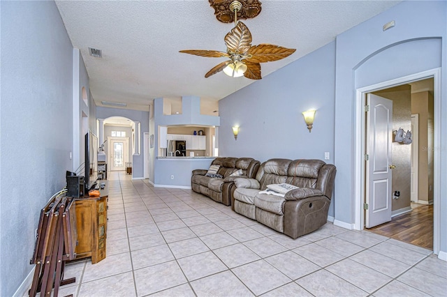 living room featuring ceiling fan, vaulted ceiling, a textured ceiling, and light tile patterned floors